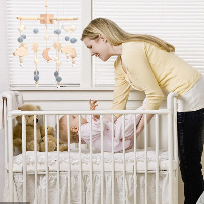 Bébé se faisant coucher dans son berceau par sa maman et son mobile pour bébé bleu suspendu
